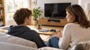 Mère assise sur un canapé discutant calmement avec son fils adolescent, une manette posée sur la table basse du salon