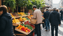 Homme de dos choisissant des agrumes sur un étal de marché, un panier en osier au bras