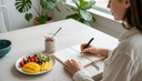 Vue plongeante sur des mains notant un journal alimentaire près d'une assiette de fruits coupés