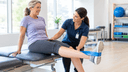 Kinésithérapeute guidant un adulte lors d'un exercice de renforcement du genou avec une bande élastique en clinique