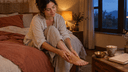 Personne assise au bord du lit massant ses pieds à l'huile de sésame tiède, bol en laiton et lait chaud sur la table de nuit