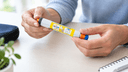 Mains adultes tenant calmement un stylo auto-injecteur d'adrénaline, illustration du geste d'urgence face au choc anaphylactique