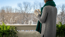 Personne de dos sur un balcon enfilant des gants de laine, écharpe et mug fumant sur la rambarde