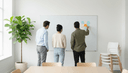 Trois collègues de dos devant un tableau blanc où un coach place une note adhésive vierge