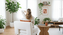 Femme assise dans un fauteuil de dos, une main sur la nuque, ordinateur fermé et tasse sur la table