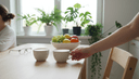 Deux tasses sur une table de cuisine, une main glissant l'une des tasses vers la chaise vide