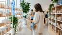 Femme de dos dans un rayon comparant deux pots de crème sans étiquette, panier au bras devant les étagères