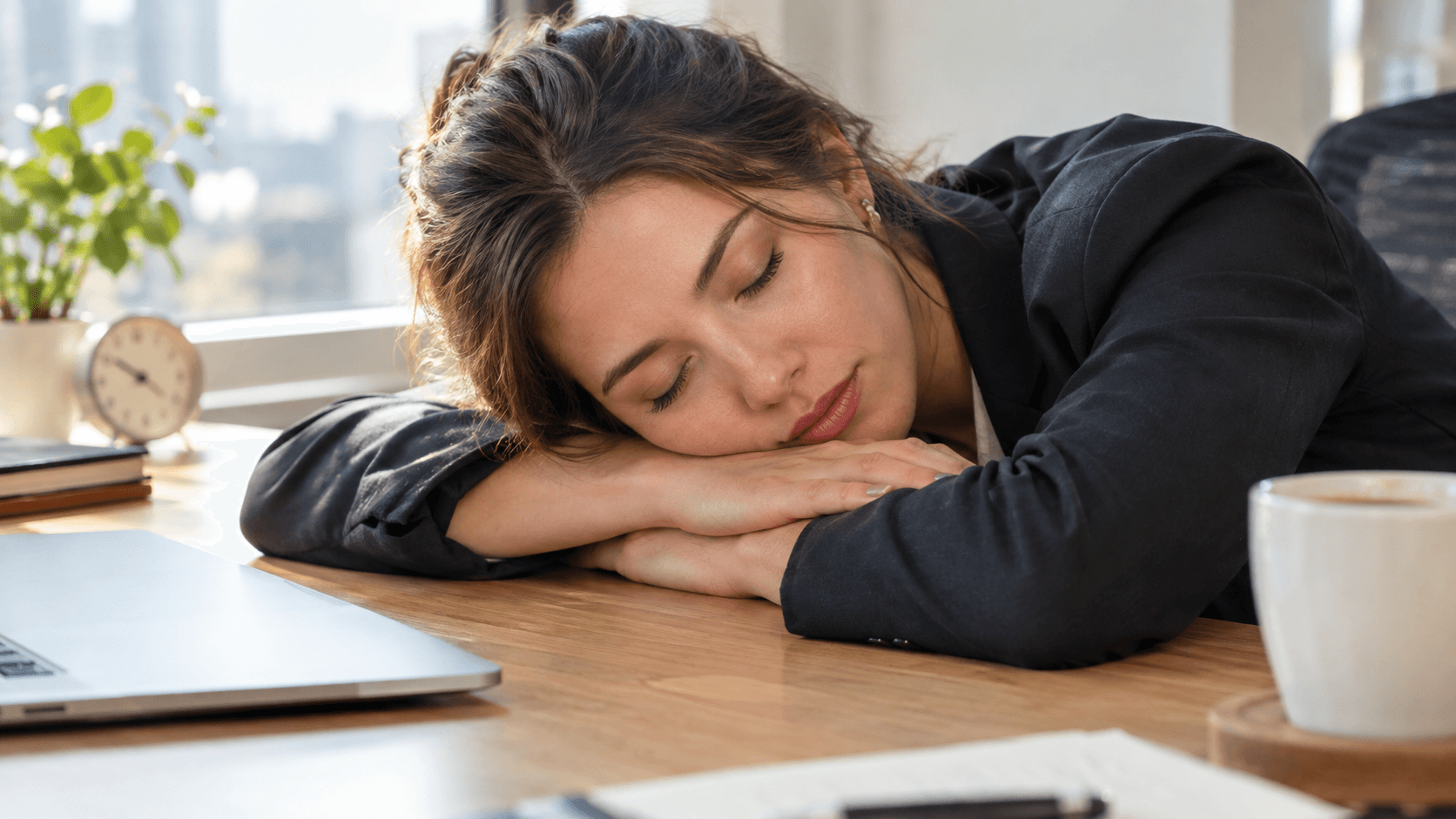 Jeune femme faisant une courte sieste réparatrice, tête posée sur ses bras à son bureau en début d'après-midi, lumière douce