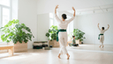 Une femme de dos ouvre les bras en plein mouvement, pieds nus, dans un studio de danse