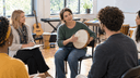 Étudiante en musicothérapie jouant d’un tambour face à un pair, observée par un formateur dans une salle lumineuse