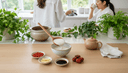 Vue plongeante sur des mains servant un congee entouré de baies de goji, de gingembre et de jujubes