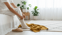 Gros plan de mains enfilant une chaussette en coton, assis au bord d'un lit près d'une couverture