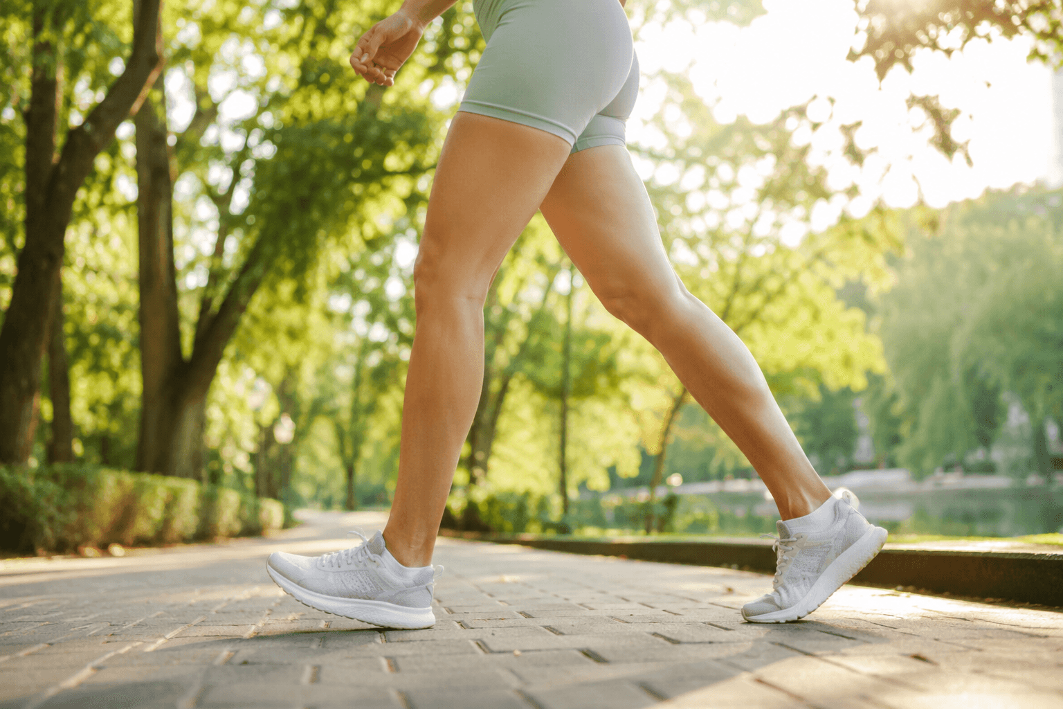Personne marchant en plein air dans un parc ensoleillé, jambes en mouvement, pour stimuler le retour veineux et la circulation sanguine