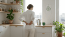 Femme de dos au plan de travail, une main sur le bas du dos, calendrier mural et tasse près d'elle