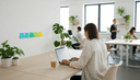 Femme de dos fermant son ordinateur portable, post-it sur le mur et tasse de café sur le bureau