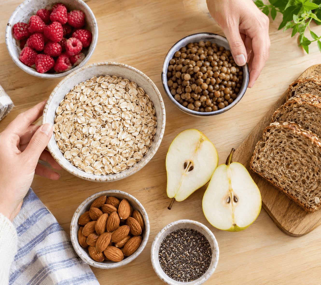 Aliments riches en fibres vus de dessus sur un plan de travail en bois : avoine, lentilles, framboises, poire et amandes