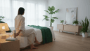 Une femme de dos assise au bord de son lit pose un tube de granules sur la table de nuit