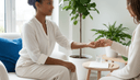 Gros plan sur la main d'un praticien tenant le poignet tendu d'une cliente assise, carnet sur la table