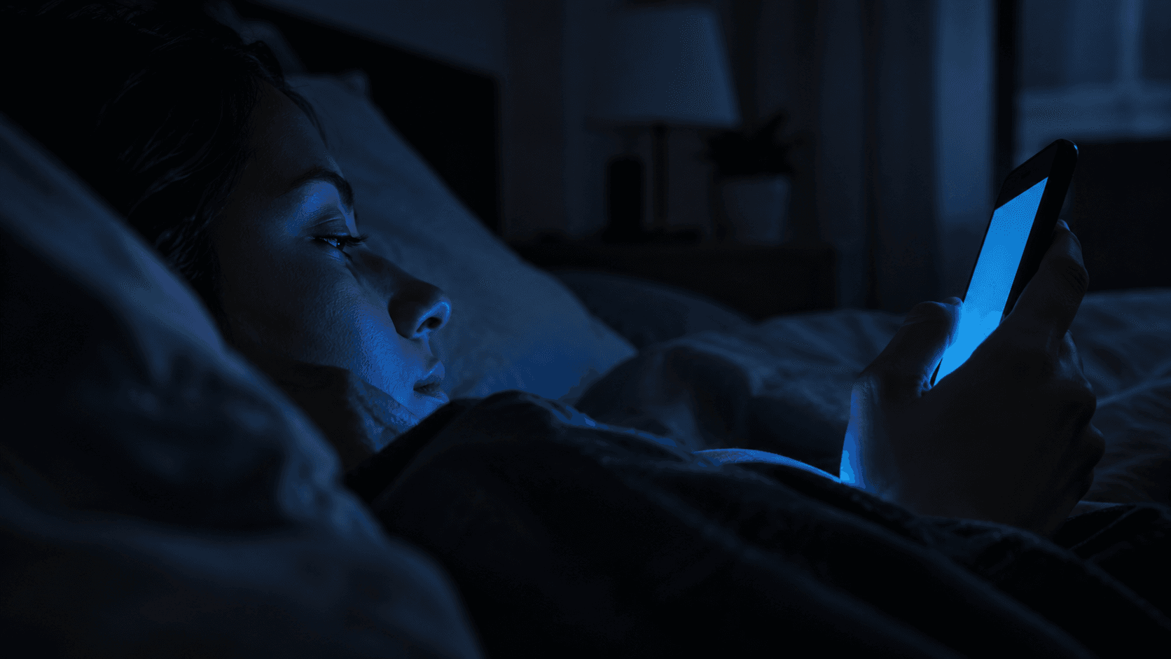 Visage éclairé par la lumière bleue d'un smartphone dans une chambre sombre, ambiance nocturne liée au sommeil