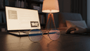 Lunettes à verres ambrés anti-lumière bleue posées sur un bureau en bois près d'un écran d'ordinateur allumé le soir