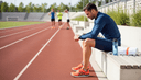 Coureur assis de profil sur un banc de stade, avant-bras sur les genoux, chronomètre à côté
