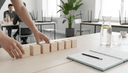 Mains alignant cinq blocs de bois sur une table d'atelier, carnet ouvert et crayon posés à côté