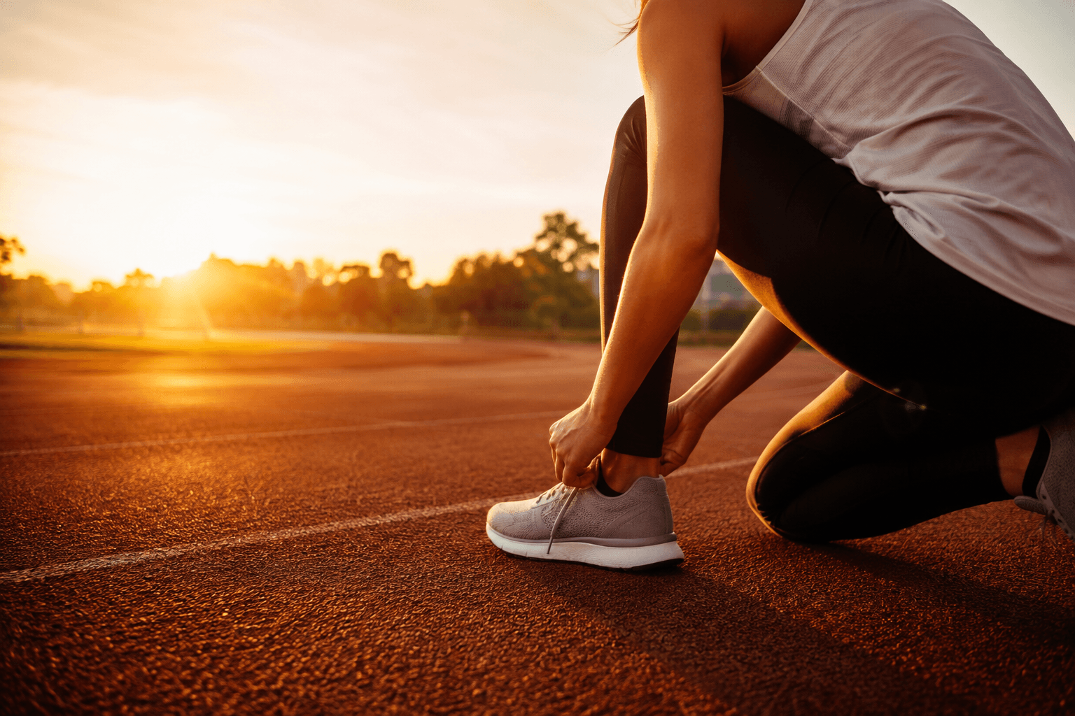 Coureur nouant ses chaussures à l'aube sur une piste d'athlétisme, ambiance chaleureuse et motivante évoquant le monologue intérieur positif et la performance