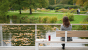 Femme vue de dos sur un banc de passerelle, regardant des feuilles dériver sur la rivière