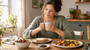 Femme sereine dans une cuisine lumineuse, tasse de thé en main, devant du pain beurré, des fruits rouges et du chocolat