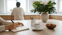Mains écrivant dans un carnet ouvert à la table de la cuisine, près d'une tasse de thé