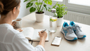 Vue plongeante sur des mains cochant une routine dans un agenda, chaussures et gourde sur la table