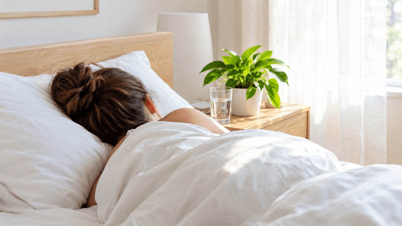 Personne endormie de dos sous une couette dans une chambre claire au petit matin, verre d'eau sur la table de chevet